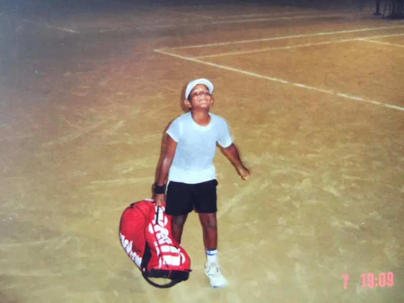 Young Anish looking up from a tennis court with his racket bag